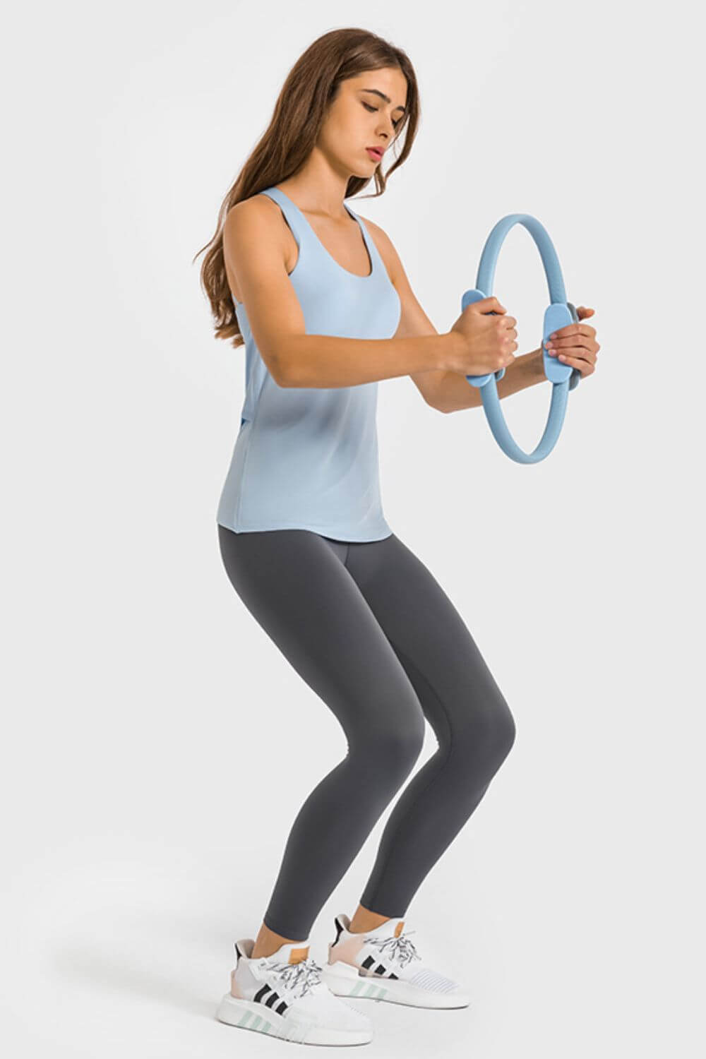 Woman in light blue tank and dark leggings using a fitness ring, showcasing activewear style and workout focus.