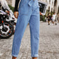 Woman wearing Bella Road Tied Straight Jeans with Pockets and white sneakers, holding a magazine while standing on a cobblestone street.