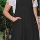 Woman wearing a sleeveless tiered midi dress in black, standing outdoors with greenery in the background.