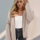 Trendy woman wearing a Double Take Contrast Open Front Dropped Shoulder Cardigan in stylish beige for relaxed chic look.