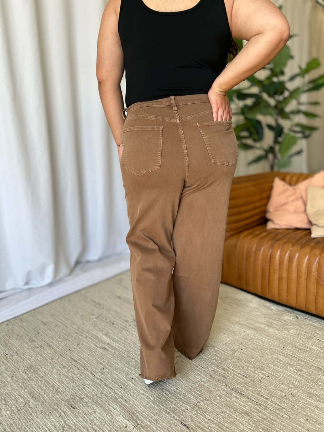 Woman wearing RFM Full Size High Rise Garment Dye Wide Leg Jeans in brown, showcasing back and relaxed fit, paired with black top.