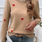 Woman wearing Devine Lace Detail Heart Long Sleeve Sweater in beige with red heart details, paired with jeans.