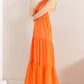 Model wearing a bright orange halter neck maxi dress with a tiered silhouette and a straw hat, perfect for summer outings.