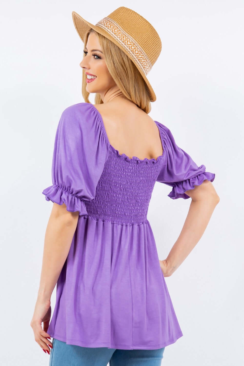 Woman wearing purple Ruffled Short Sleeve Smocked Blouse with delicate ruffles and smocked waist, paired with a straw hat.