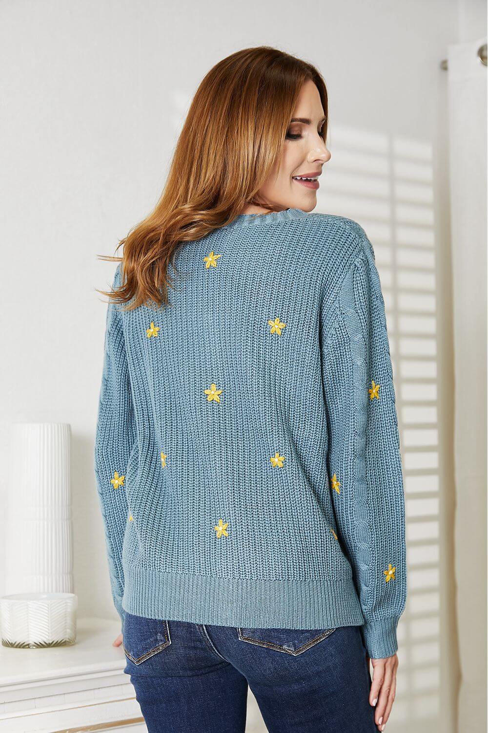 Woman wearing HEYSON floral embroidered cable cardigan in blue, showcasing intricate yellow flower designs and cozy knit texture.