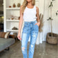 Woman wearing distressed straight Judy Blue Jeans with patch pockets, paired with a white blouse, standing in a chic room.