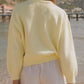 Woman wearing Bella Road Button Down Long Sleeve Cardigan in pastel yellow by the beach, showcasing its cozy design.