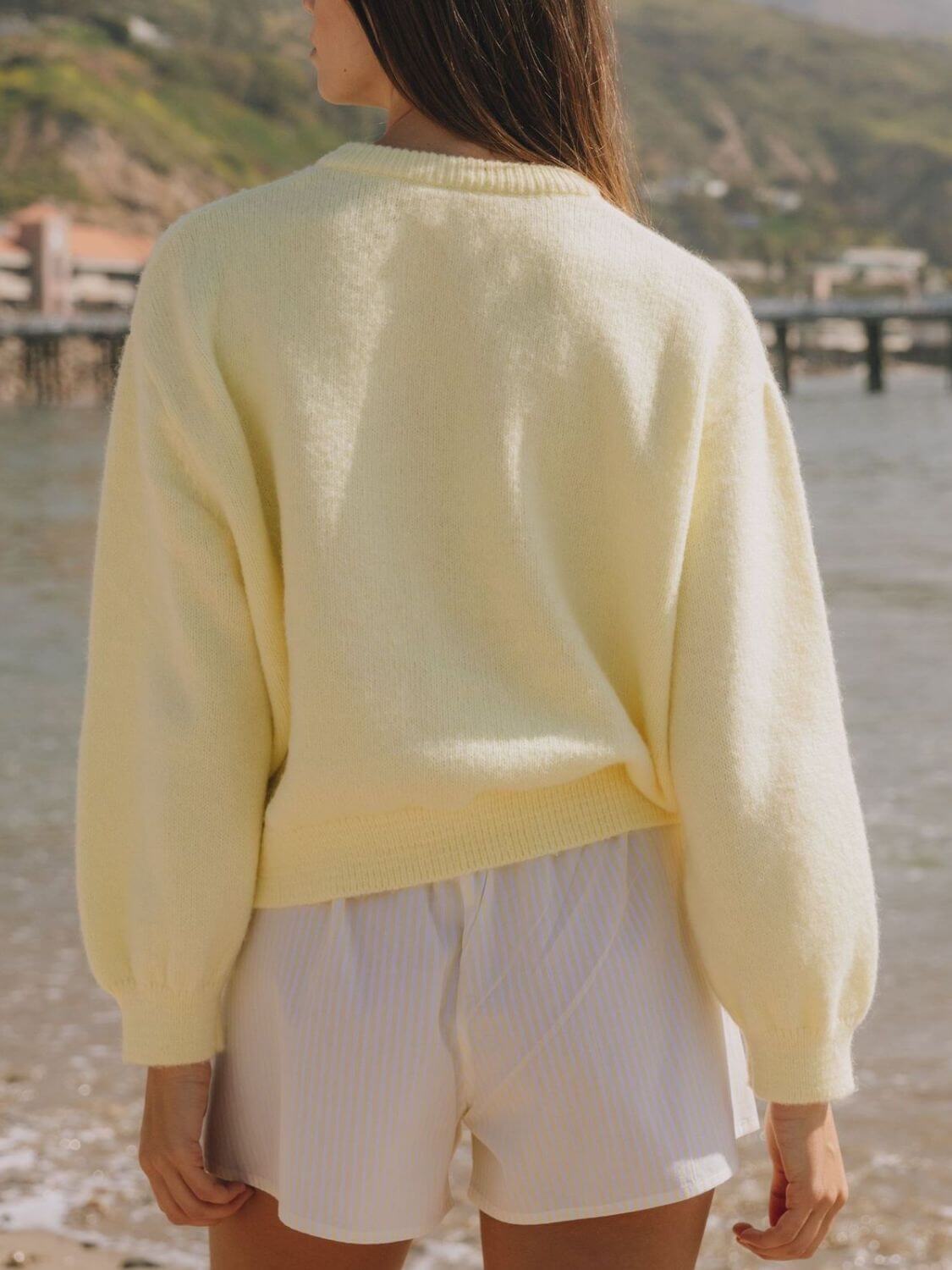 Woman wearing Bella Road Button Down Long Sleeve Cardigan in pastel yellow by the beach, showcasing its cozy design.