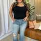 Woman wearing Judy Blue medium rise tummy control flare jeans with distressed detailing, standing casually indoors.