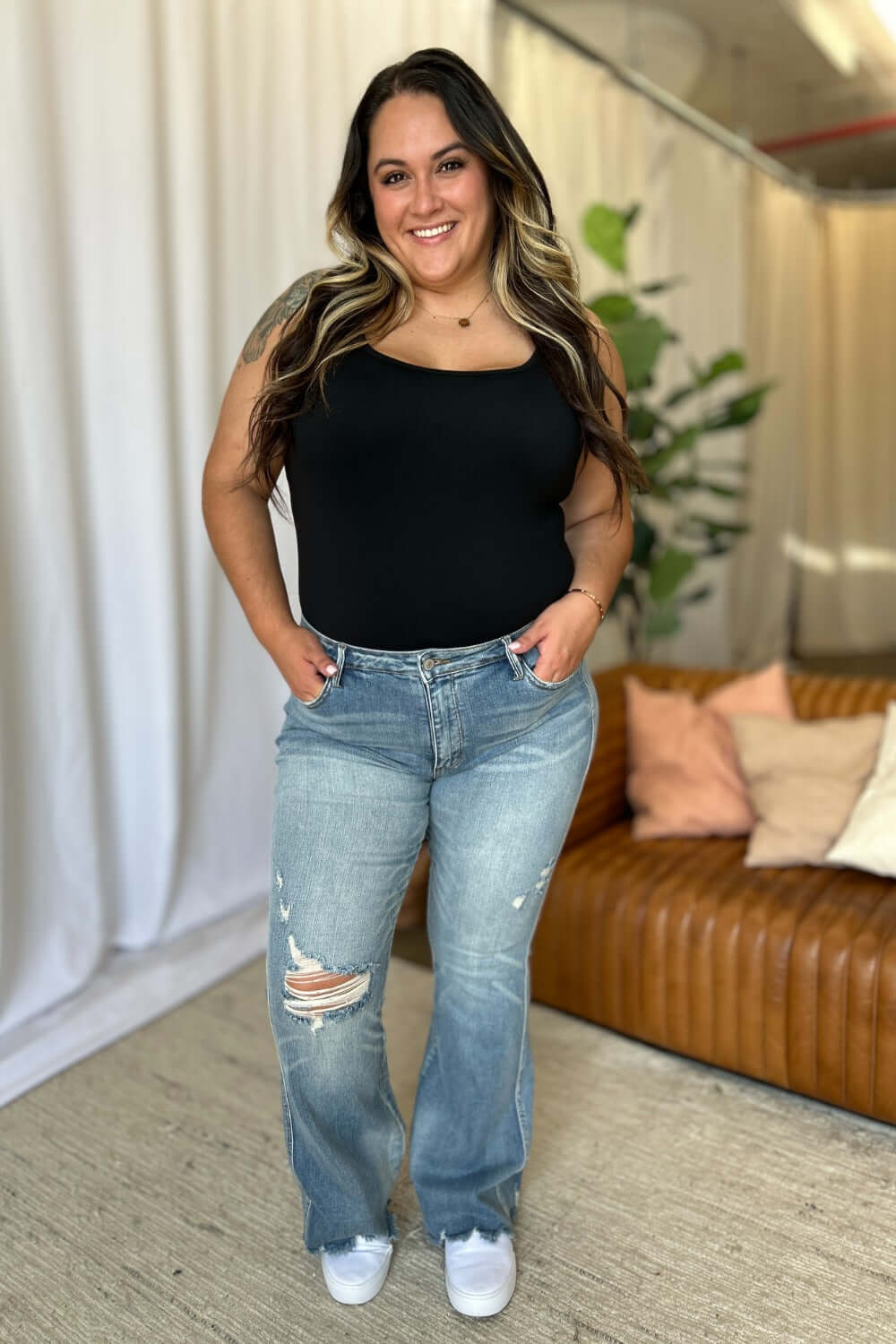 Woman wearing Judy Blue medium rise tummy control flare jeans with distressed detailing, standing casually indoors.