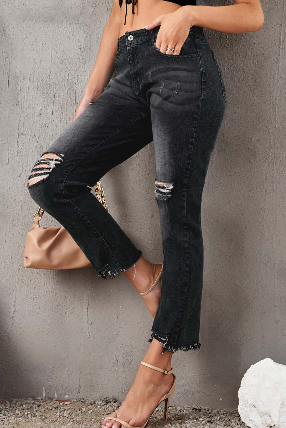 Woman wearing stylish distressed cropped jeans in black with a solid pattern, featuring rips and slightly stretchy material.