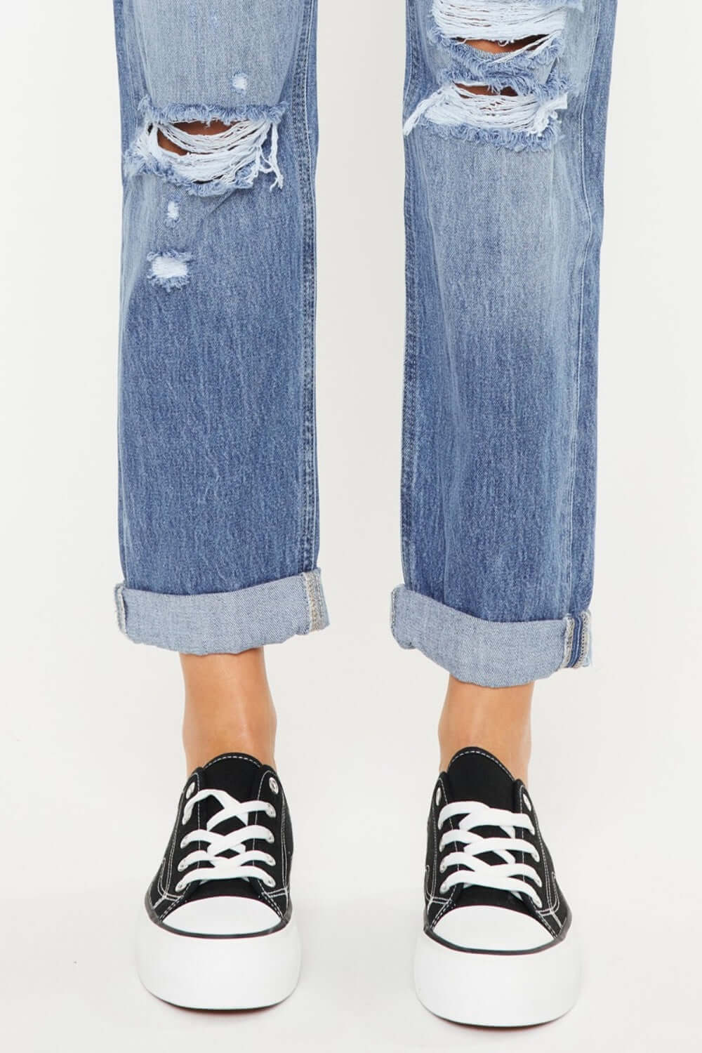 Mid rise distressed straight jeans with cuffed hems and black sneakers for a trendy, casual look.