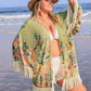 Plus size woman in floral fringe cover-up enjoying the beach with a straw hat and a playful pose.