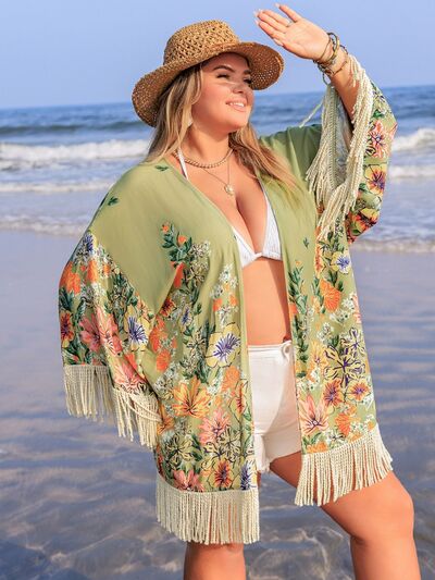 Plus size woman in floral fringe cover-up enjoying the beach with a straw hat and a playful pose.