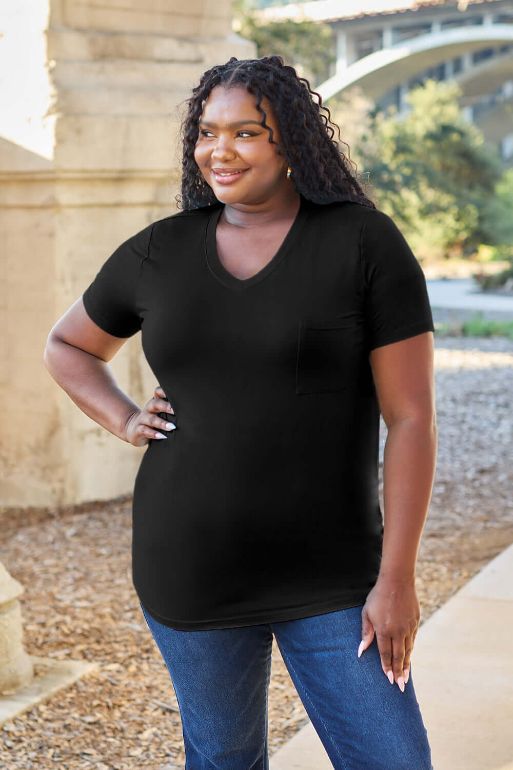 Woman wearing Basic Bae Bamboo V-Neck Short Sleeve T-Shirt in black, standing outdoors.