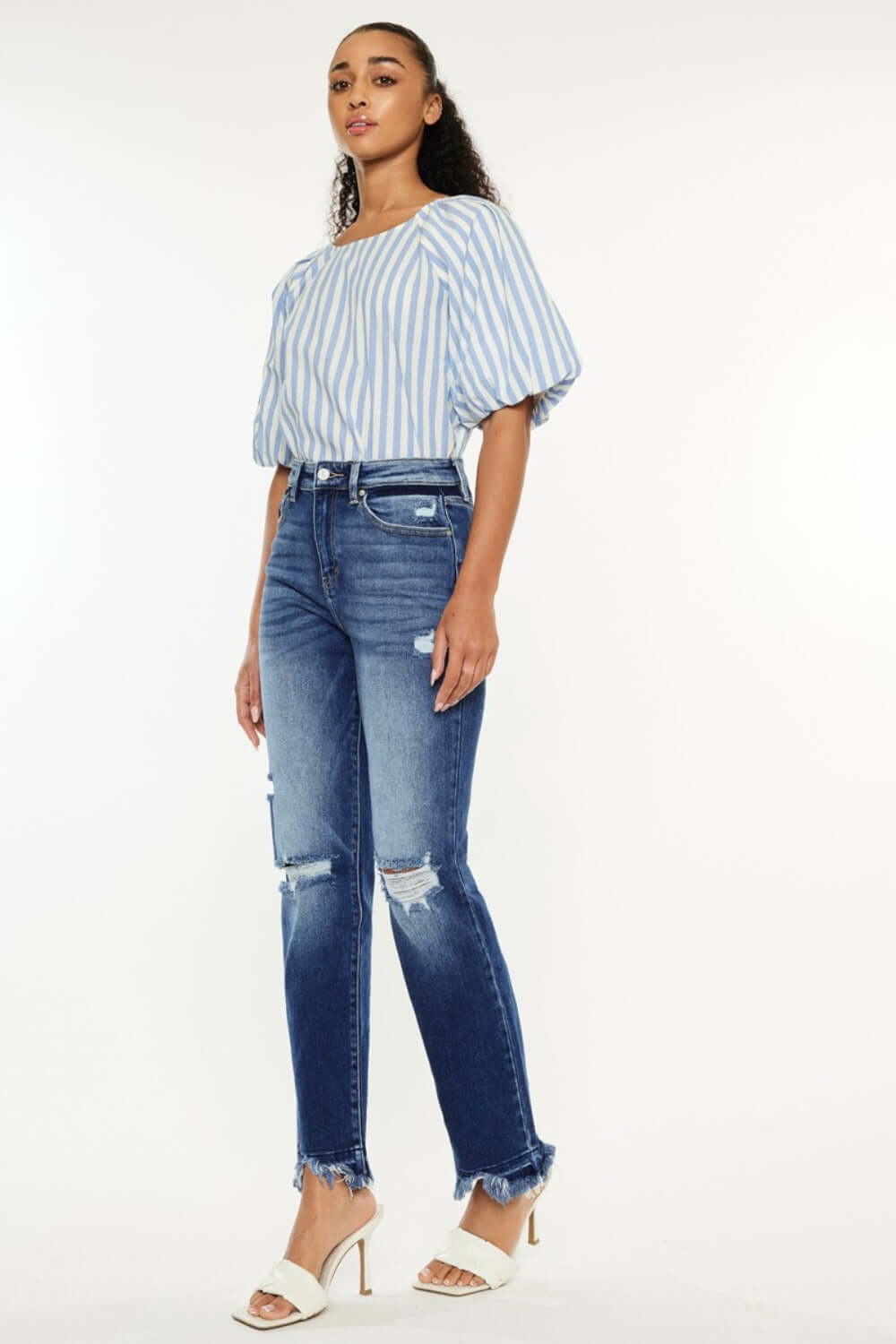 Woman wearing Kancan High Rise Distressed Slim Straight Jeans with frayed hem and striped blouse, showcasing trendy and versatile style.