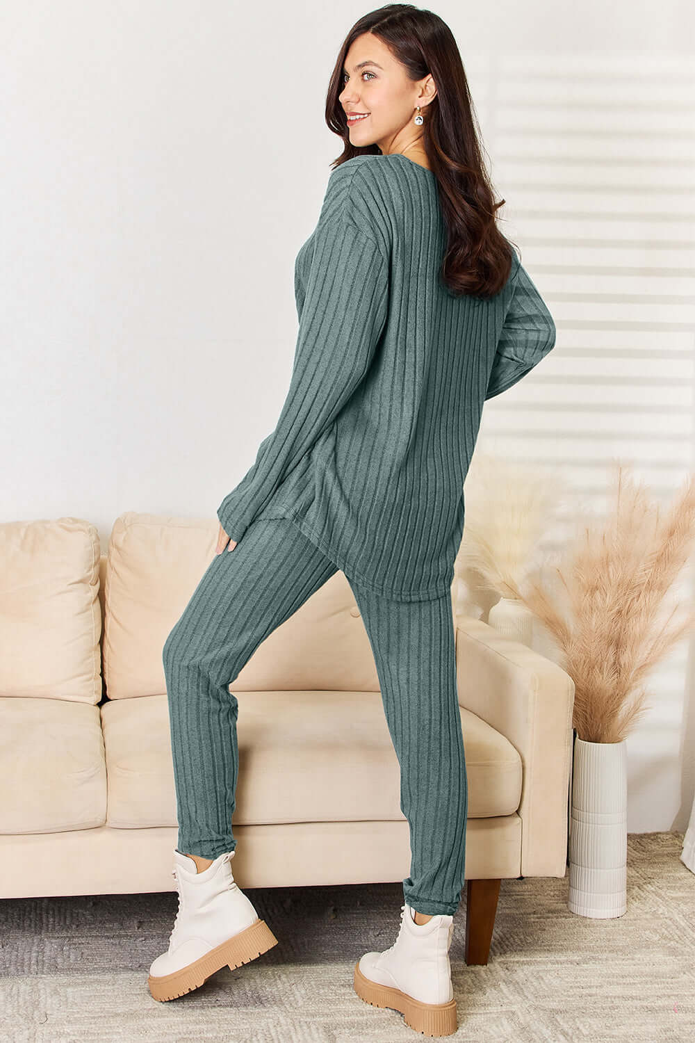 Woman wearing ribbed notched long sleeve top and pants set in green, standing in living room with beige sofa and decor.