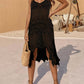 Woman wearing Openwork Scoop Neck Spaghetti Strap Cover-Up Dress in black, holding a straw bag, standing outdoors with beach background