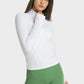 Woman in a white Millennia Half Zip Thumbhole Sleeve Sports Top and green leggings, showcasing comfort and style for yoga.