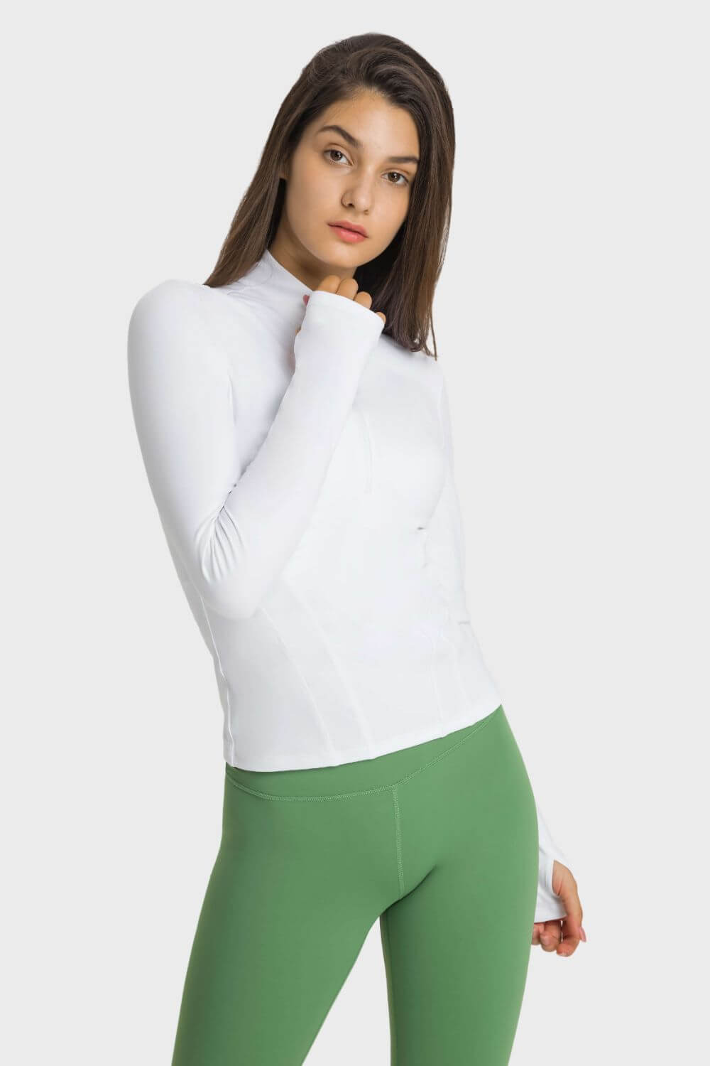 Woman in a white Millennia Half Zip Thumbhole Sleeve Sports Top and green leggings, showcasing comfort and style for yoga.