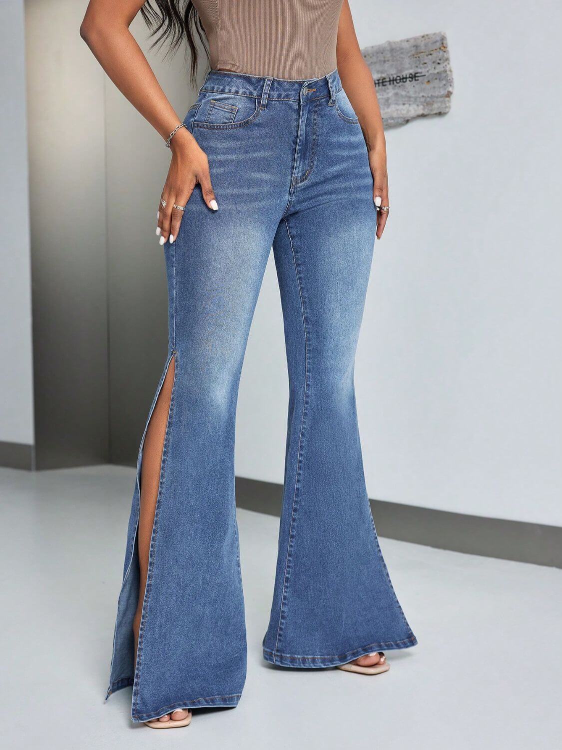 Woman wearing stylish slit flare jeans with pockets and flared leg opening, standing in a modern room. Highly stretchy denim, perfect for any occasion.