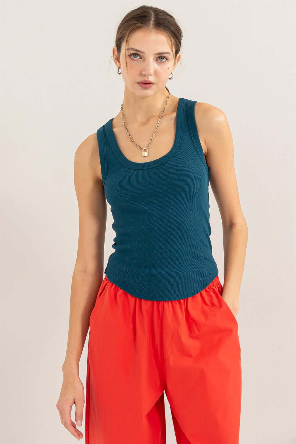 Woman wearing Ribbed Scoop Neck Racerback Tank in teal, paired with red pants, showcasing a stylish and comfortable fit.