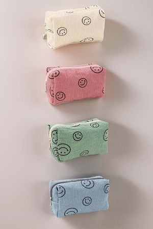 Four colorful corduroy cosmetic pouches with smiley faces in white, pink, green, and blue, perfect for organizing makeup essentials.