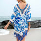 Woman wearing blue cutout V-neck three-quarter sleeve cover-up with tassels, standing on the beach near the ocean.