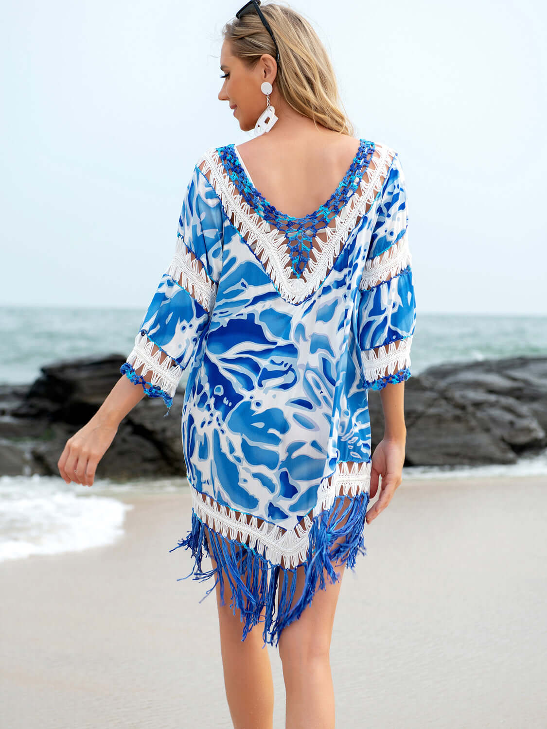 Woman wearing blue cutout V-neck three-quarter sleeve cover-up with tassels, standing on the beach near the ocean.