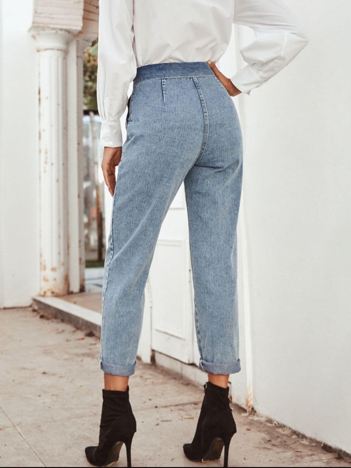 Stylish woman in light blue straight leg jeans with pockets, paired with high-heeled boots, showcasing a trendy back view.