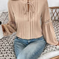 Woman wearing Perfee Frill Tie Neck Long Sleeve Blouse with ruffled details and lace sleeves, sitting on a knitted blanket.