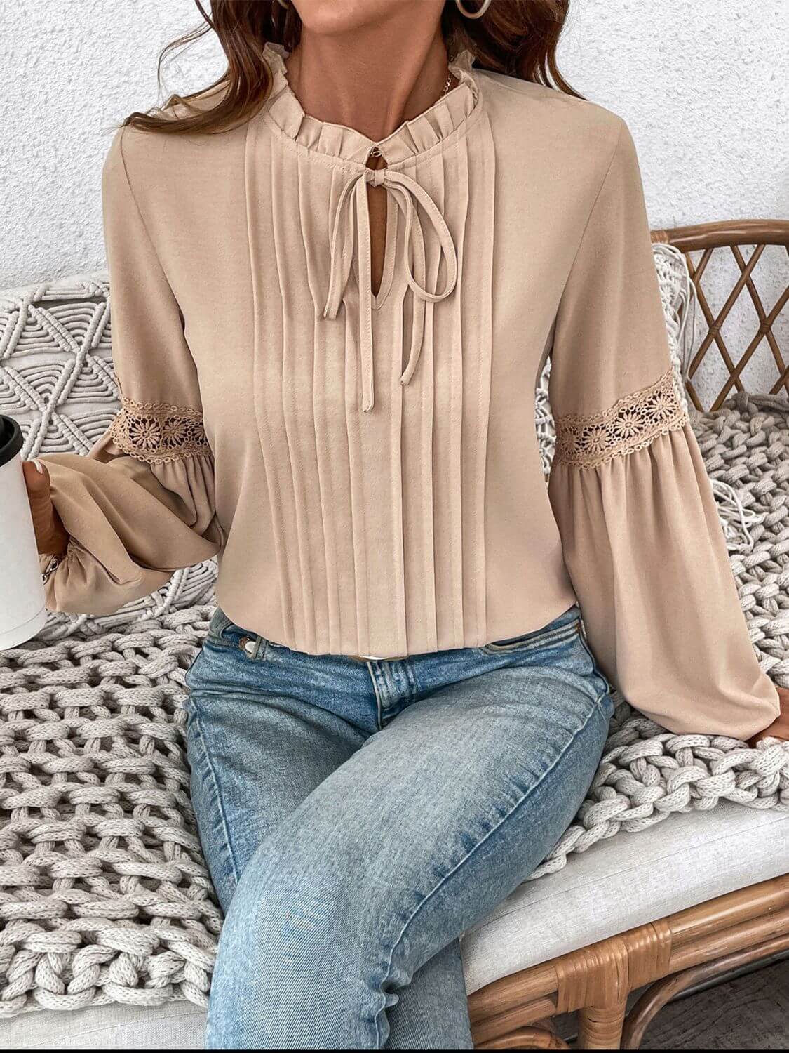 Woman wearing Perfee Frill Tie Neck Long Sleeve Blouse with ruffled details and lace sleeves, sitting on a knitted blanket.