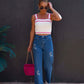 Woman wearing embroidered straight jeans with pockets and white tank top carrying a pink handbag