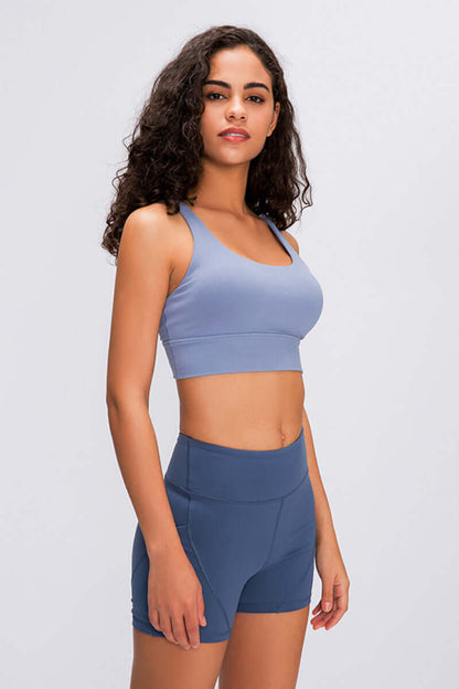 Model showcasing the Millennia Double X Sports Bra in blue, featuring a supportive design and stylish strappy back.