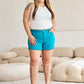 Woman wearing RFM Jeans tummy control high waist raw hem denim shorts in a stylish living room.