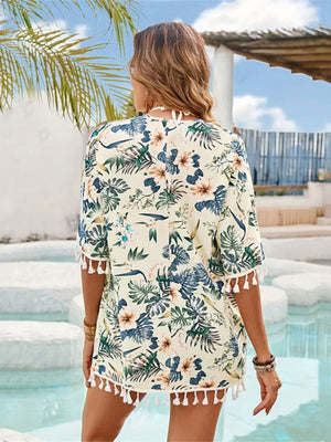 Stylish woman in pastel yellow tassel cover-up showcasing floral print by a pool under a sunny sky.