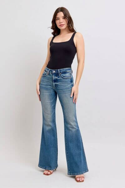 Model showcasing Judy Blue Mid Rise Tummy Control Vintage Wash Jeans paired with a black tank top, highlighting retro style.