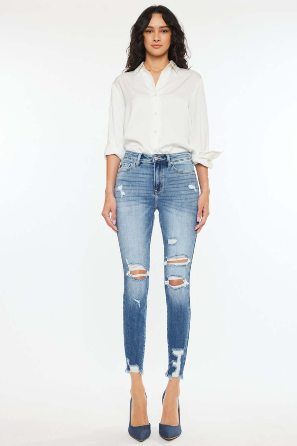 Woman wearing High Rise Frayed Ankle Skinny Jeans in medium wash with distressed detailing and fray hem, paired with white shirt and heels.