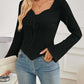 Woman wearing Bella Road Ribbed Drawstring Long Sleeve T-Shirt in black, paired with blue jeans in a modern setting.