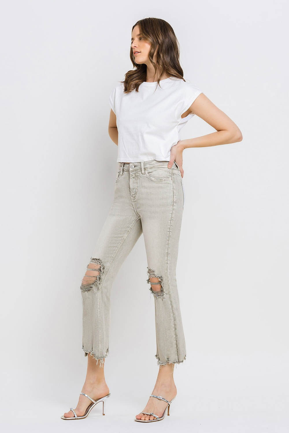 Woman wearing Lovervet Distressed Raw Hem Cropped Flare Jeans styled with white top and heeled sandals