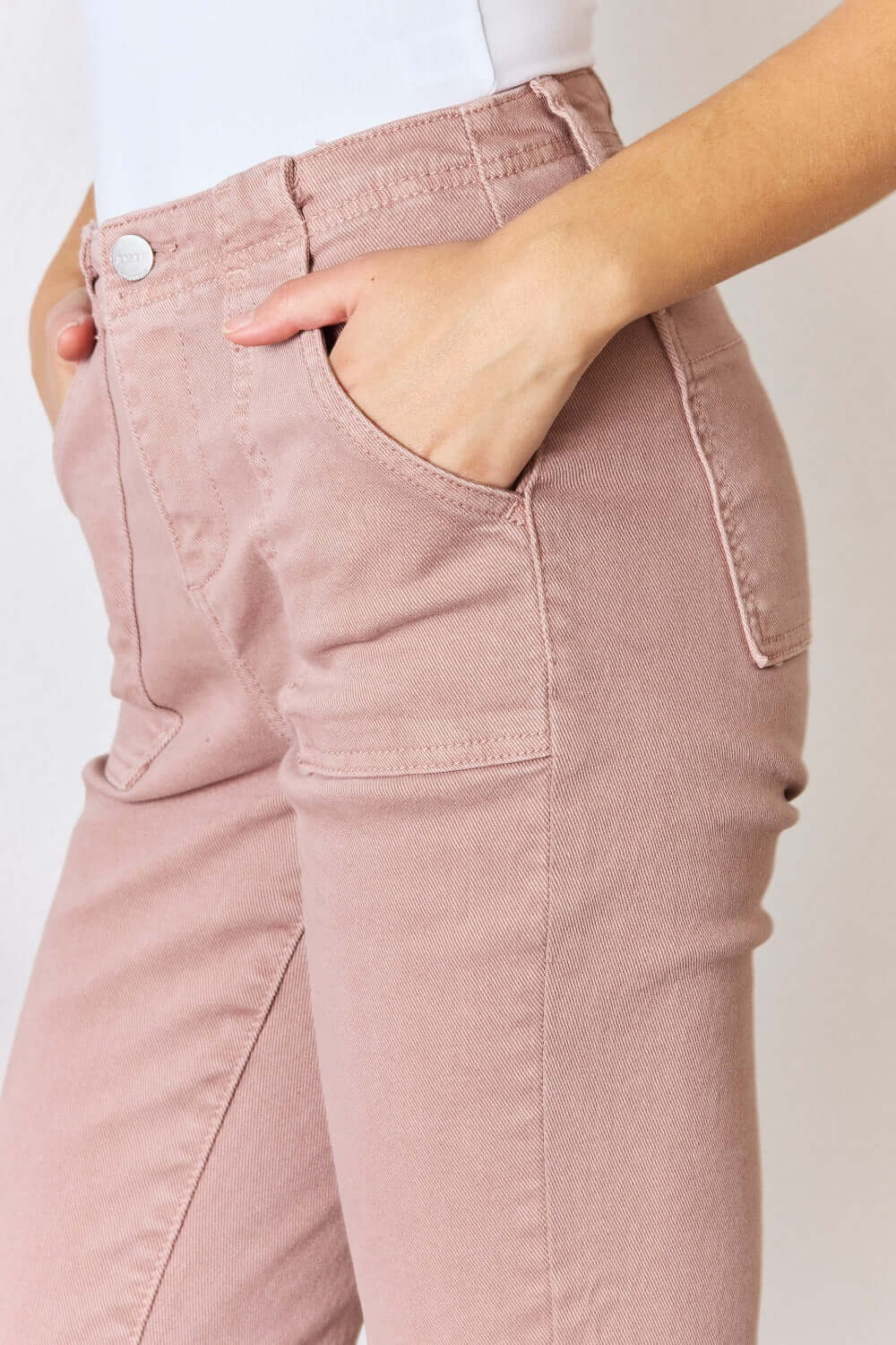 Woman wearing Risen Jeans high-rise ankle flare jeans in a stylish pink color, showcasing the flattering fit and versatile pockets.