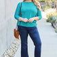 Woman wearing green round neck batwing sleeve top with blue jeans and sunglasses standing outdoors