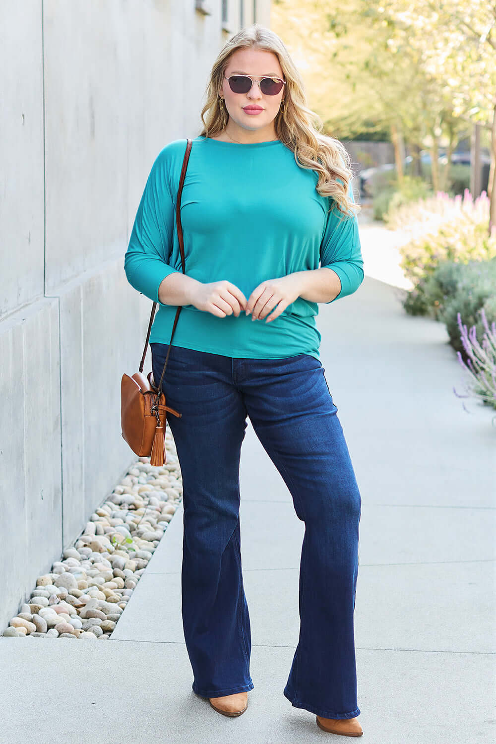 Woman wearing green round neck batwing sleeve top with blue jeans and sunglasses standing outdoors