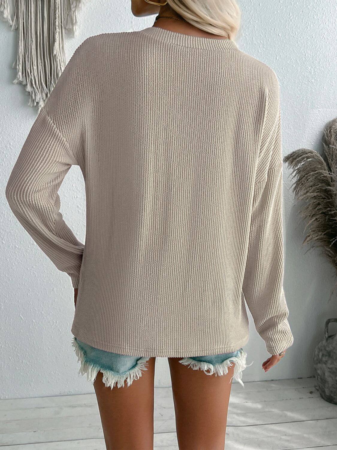 Beige textured V-neck long sleeve T-shirt with pockets, seen from the back, worn with frayed denim shorts, perfect for casual wear.