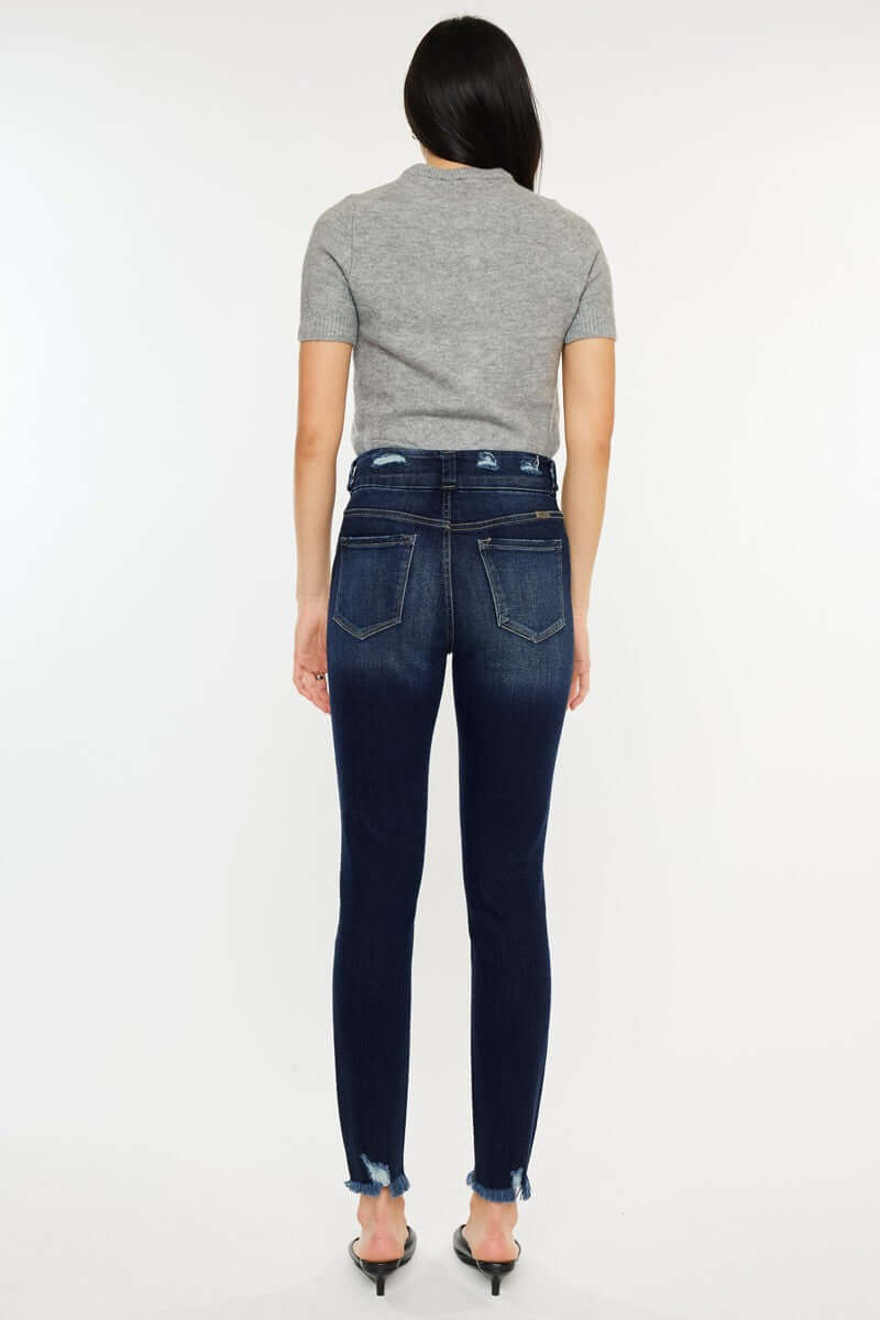 Back view of model wearing Cat's Whiskers Raw Hem High Waist Jeans in dark wash, paired with a grey t-shirt and black heels.