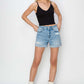 Stylish woman in Risen Jeans distressed mid-rise waist denim shorts, paired with a black tank top and white boots