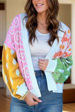 Woman wearing a colorful color block open front long sleeve cardigan with pink, yellow, green, and blue patterns.