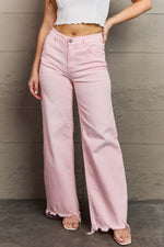 Light pink Raelene High Waist Wide Leg Jeans by Risen Jeans modelled against a gray wall, showcasing flattering fit and retro wide leg design.