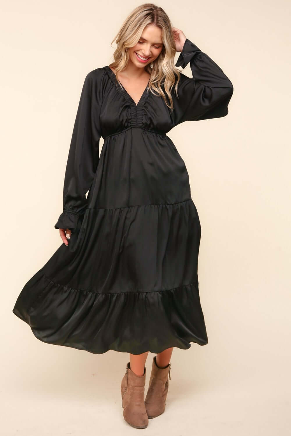 Woman wearing black flounce sleeve tiered midi dress with pockets, complemented by brown ankle boots.