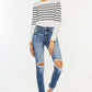 Model wearing high waist distressed raw hem ankle skinny jeans with striped long-sleeve top and white sneakers, trendy and edgy fashion look